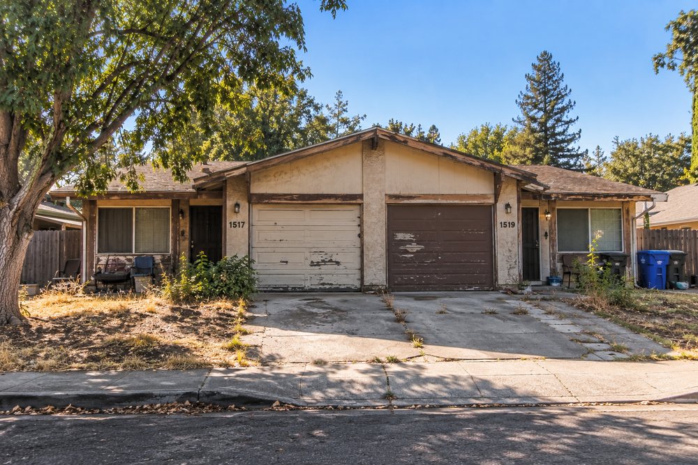 Older duplex with peeling paint, a cracked driveway and overgrown landscaping, representative of deferred-maintenance properties Dottco purchases as-is