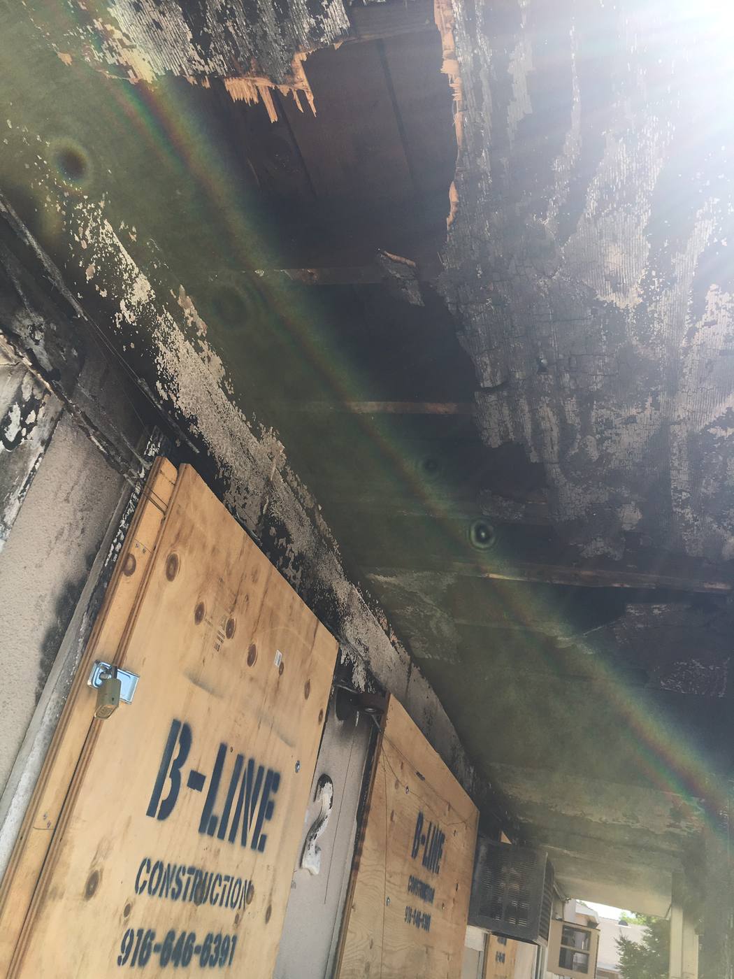 The Sacramento sixplex before rehabilitation: fire-burned breezeway ceiling with charred rafters, unit doors boarded over with plywood and padlocked